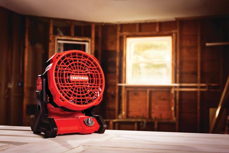 Ventilateur de chantier sans fil rouge et noir Craftsman CMCE001B sur un établi dans une pièce en construction.