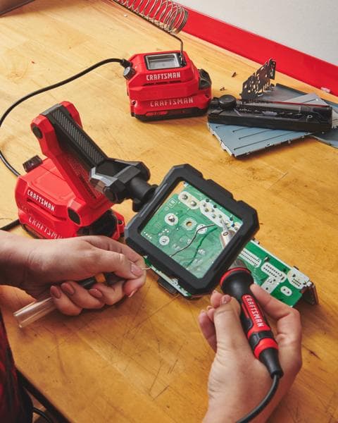 Photo du fer à souder sans fil CRAFTSMAN CMCE040B utilisé pour souder une carte de circuit sur un établi en bois.
