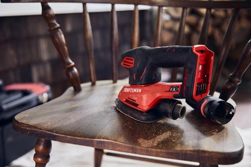 Ponceuse sans fil Craftsman CMCW221B rouge et noire posée sur une chaise en bois, avec raccord pour poussière.