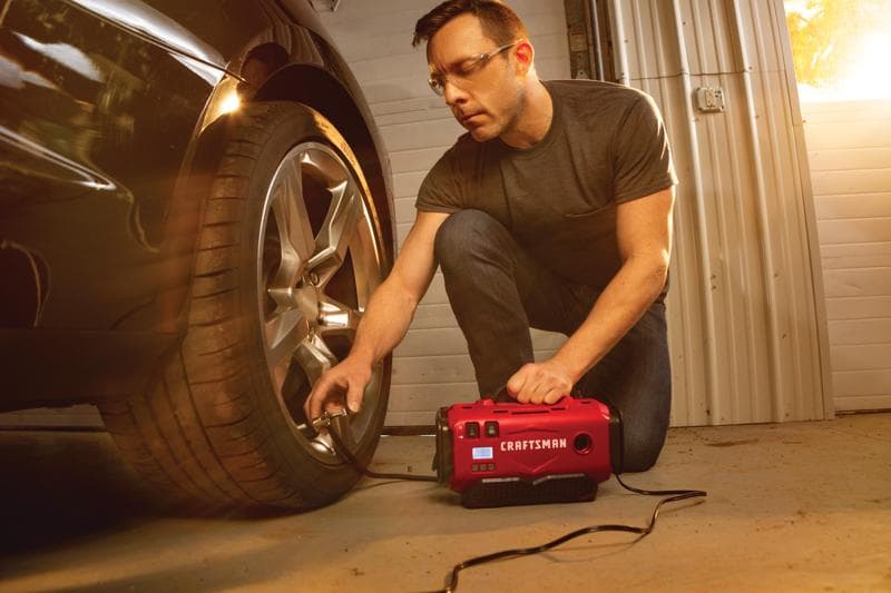 Photo du gonfleur portable Craftsman CMCE520B utilisé pour gonfler un pneu de voiture dans un garage.