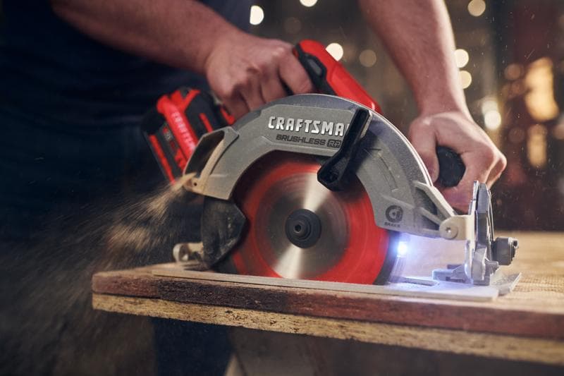 Photo de la scie circulaire sans fil CRAFTSMAN CMCS551B en utilisation, découpant du bois avec lame rouge et poussière visible.