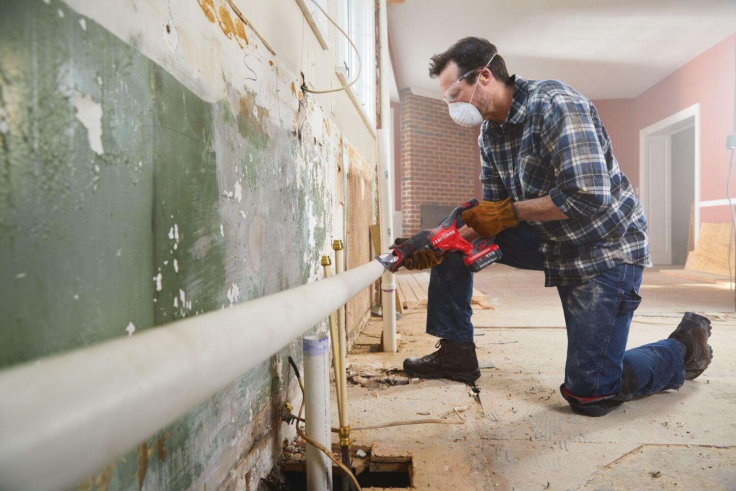 Photo of worker using CRAFTSMAN cordless reciprocating saw CMCS350B to cut a pipe during renovation, indoor setting.