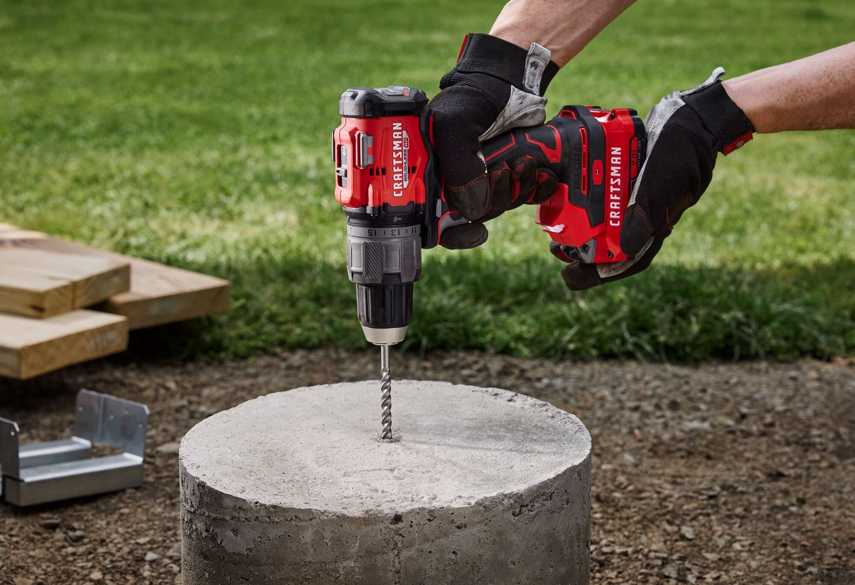 Photographie de la perceuse à percussion sans fil CRAFTSMAN CMCD726B perçant du béton à l'extérieur, tenue par des mains gantées.