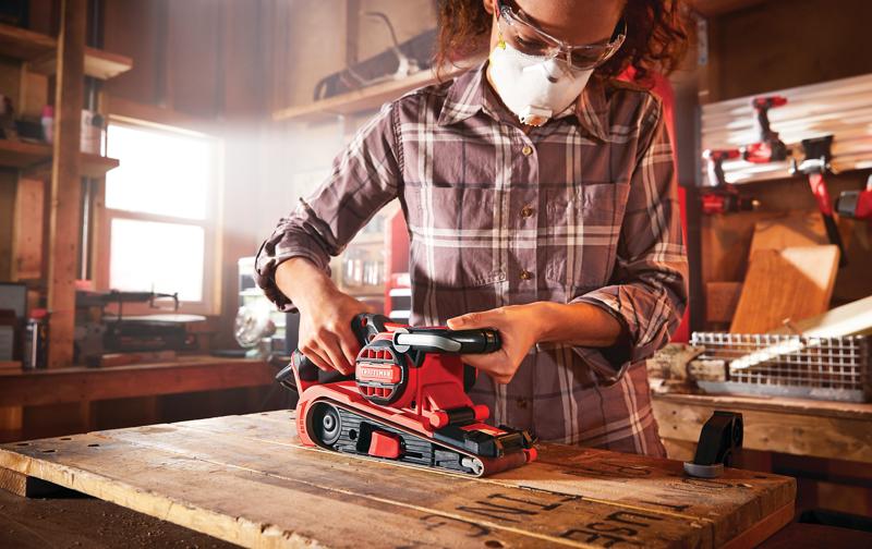 Photo of CRAFTSMAN CMEW213 belt sander in use on wood table in workshop setting.