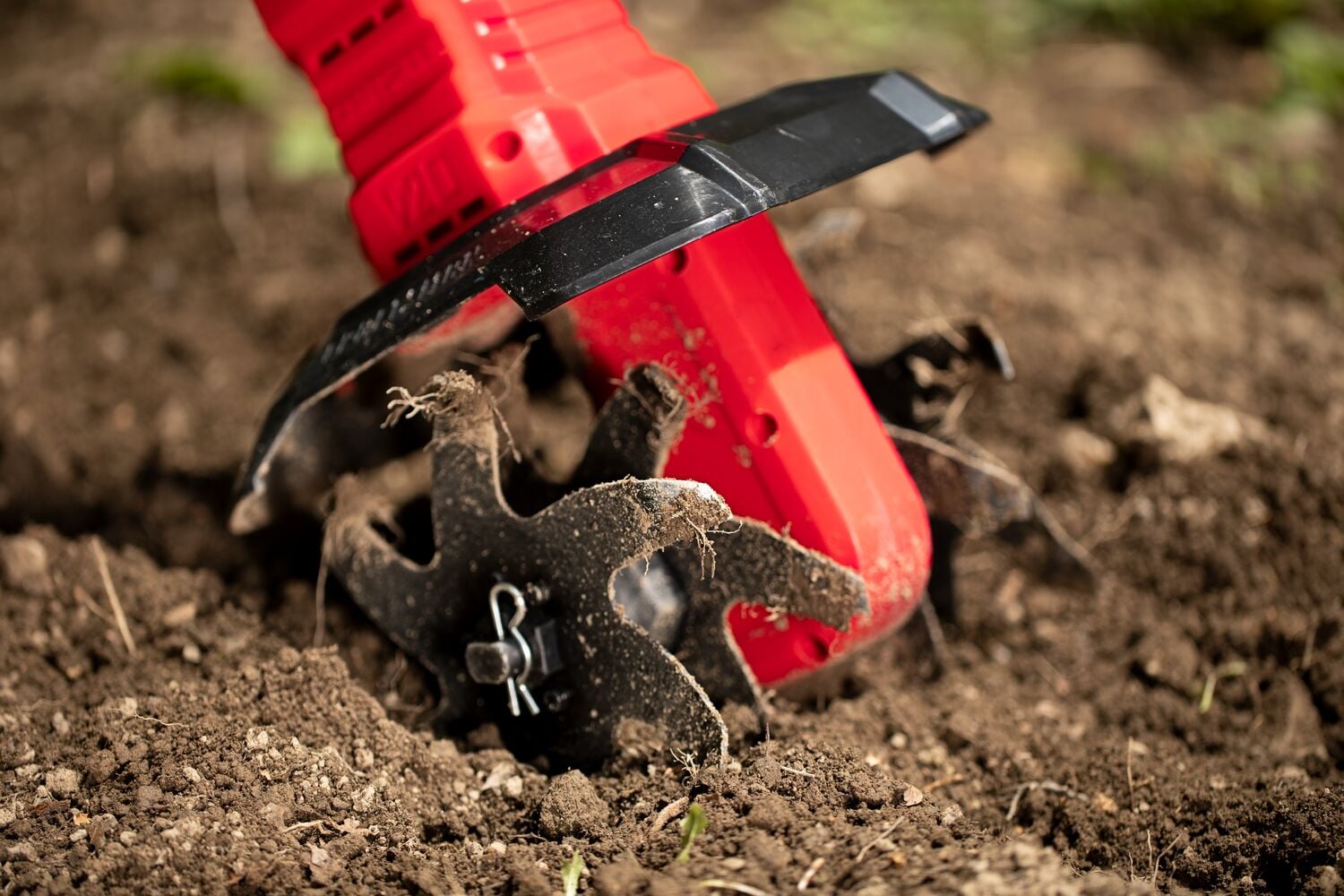 Close-up photo of Craftsman CMCTL320B cordless tiller cutting through soil, visible dirt on metal tines.