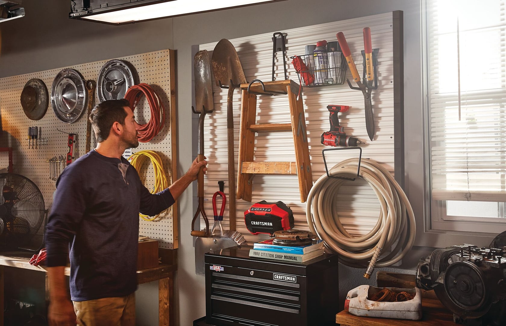 Photo of CRAFTSMAN storage system SKU CMST22000 in a garage, holding tools, hose, and a wooden ladder.
