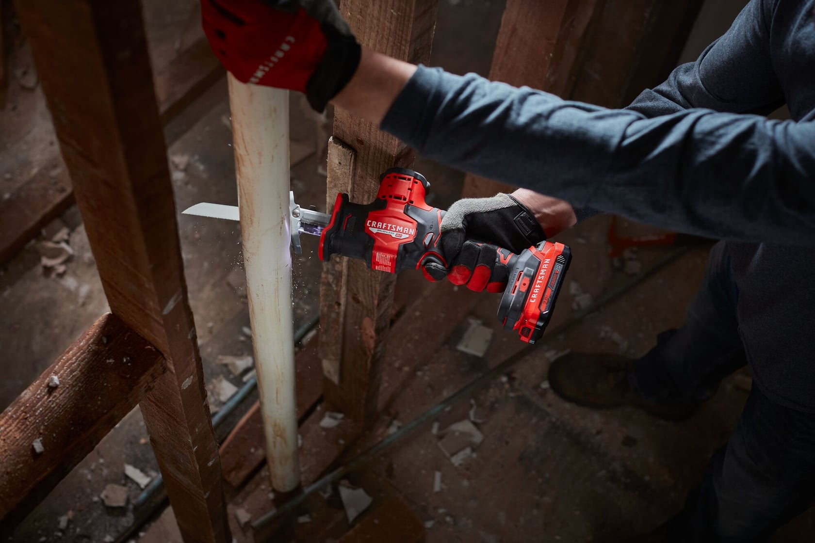 Photo of a person using a Craftsman cordless reciprocating saw, SKU CMCS340B, to cut a white PVC pipe during construction.