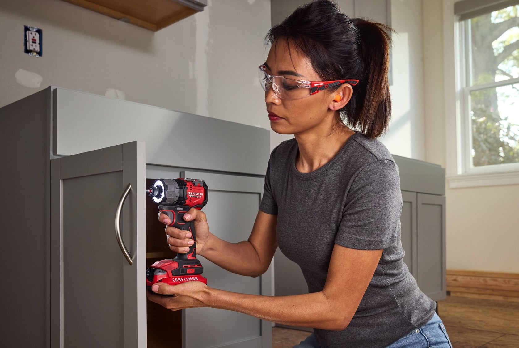 Personne utilisant une visseuse à chocs sans fil CRAFTSMAN modèle CMCF610B pour installer une poignée sur une armoire grise en intérieur.