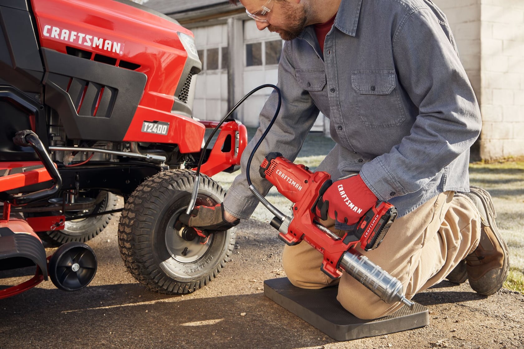 Photo of Craftsman CMCGG001D1 cordless grease gun used for maintenance on red tractor tire outdoors.