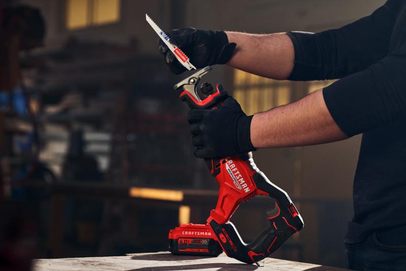 Photographie de la scie sabre Craftsman CMCS351B avec batterie, tenue par des mains gantées dans un atelier.