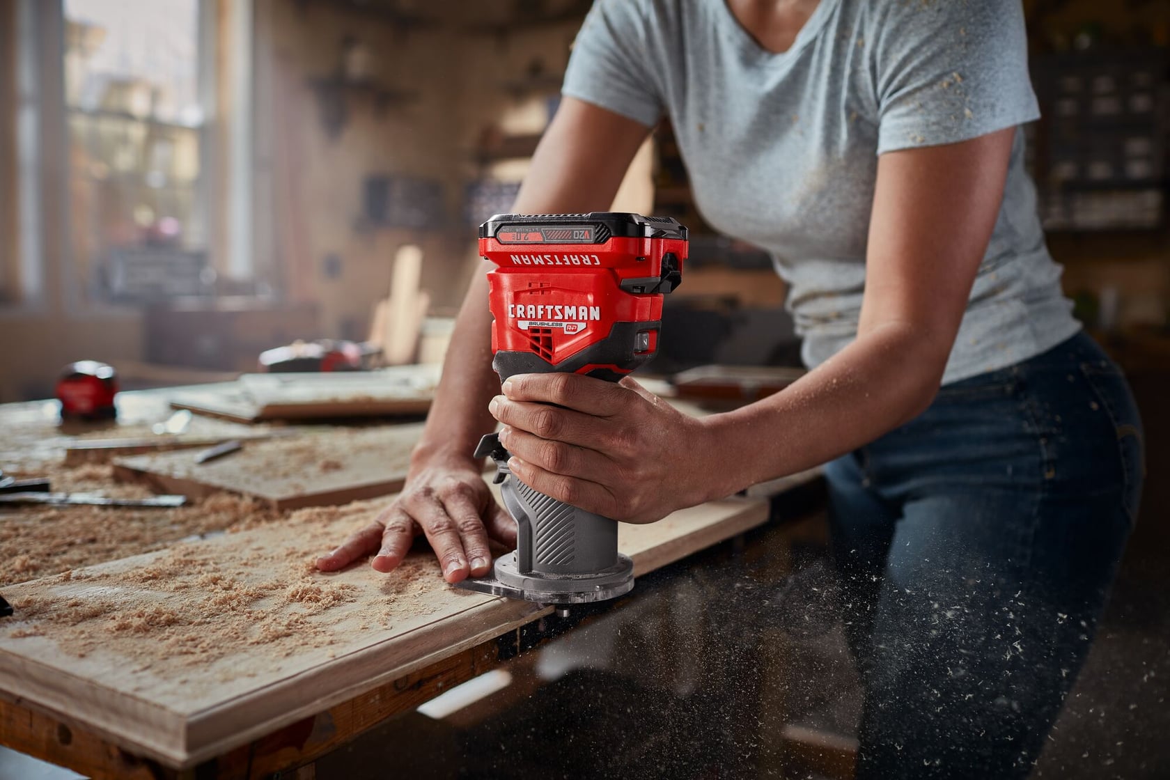 Photographie d'une personne utilisant une défonceuse compacte sans fil Craftsman, SKU CMCW400B, sur une planche en bois dans un atelier.