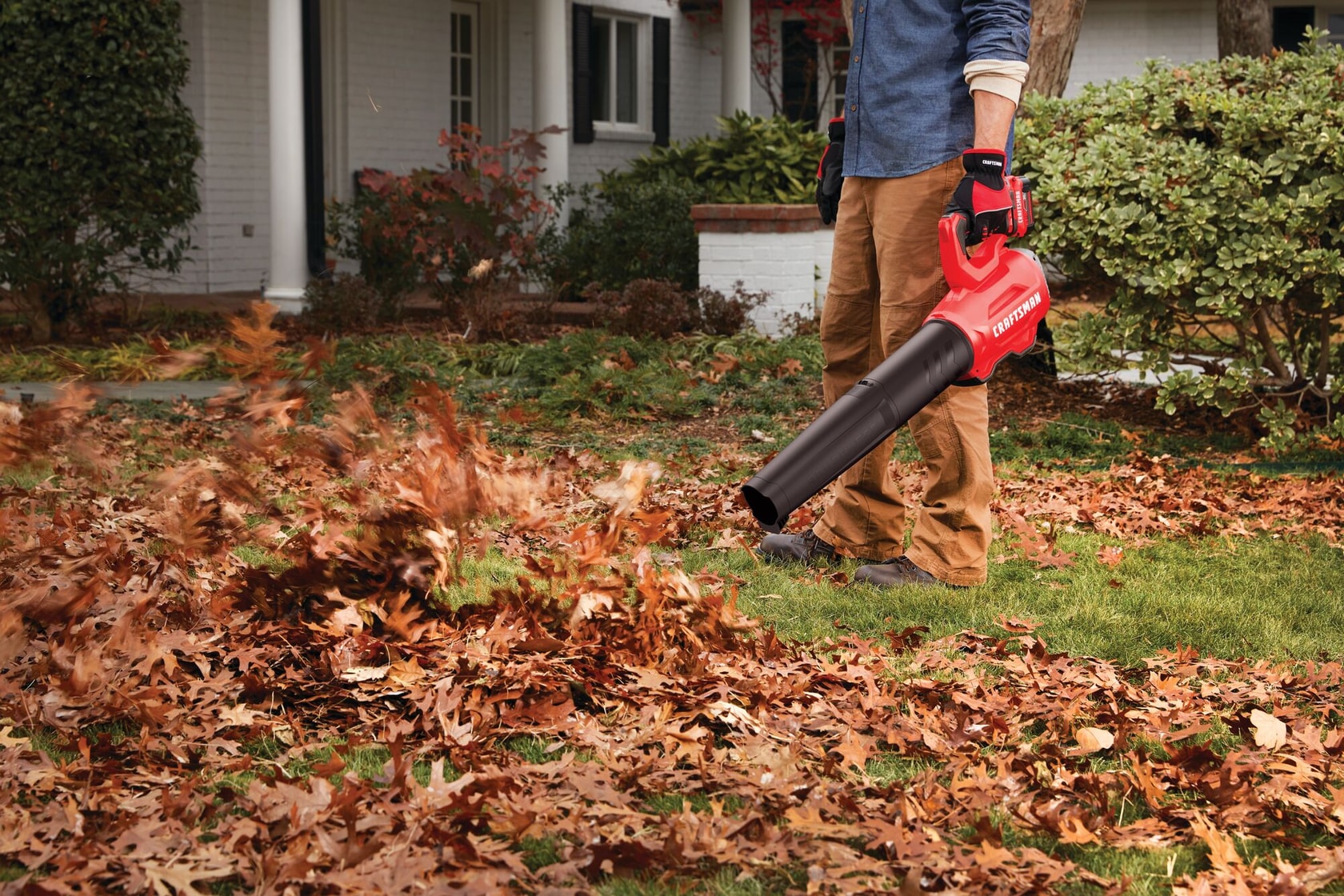 Photographie du souffleur de feuilles Craftsman SKU CMCBL720M1 en fonctionnement, nettoyant la pelouse près d’une maison.