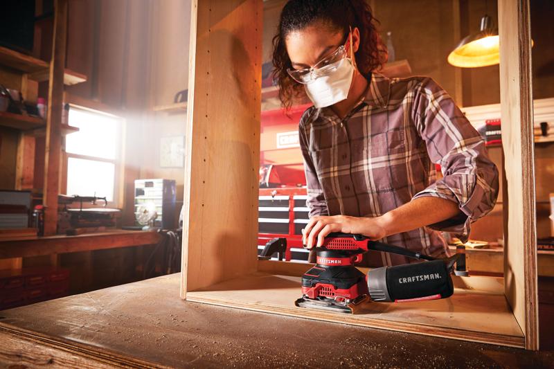 Photo de la ponceuse Craftsman CMEW230 utilisée sur du bois dans un atelier, sac à poussière attaché, mains et torse visibles.