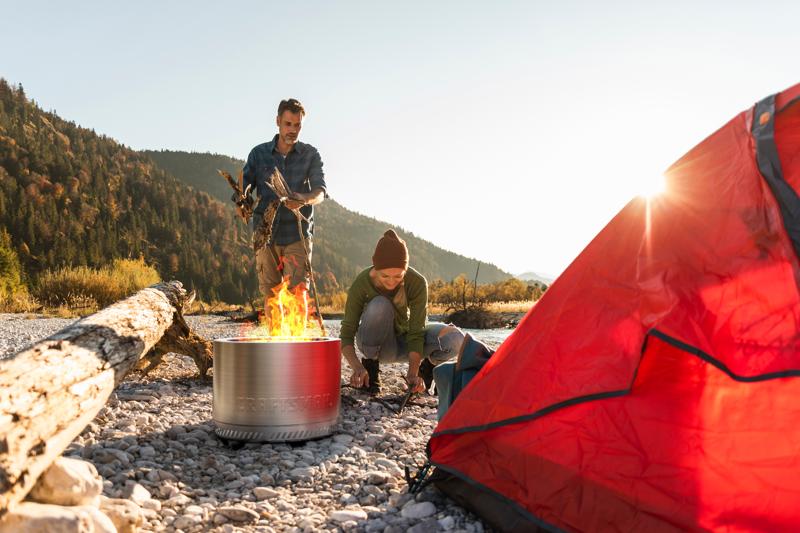 Man and woman using Craftsman fire pit at campsite