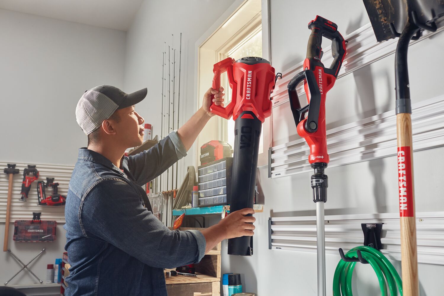 Person mounting lawn equipment on Versatrack Garage Storage System Storage Rail with 20 Piece Mounting Accessories installed on garage wall.