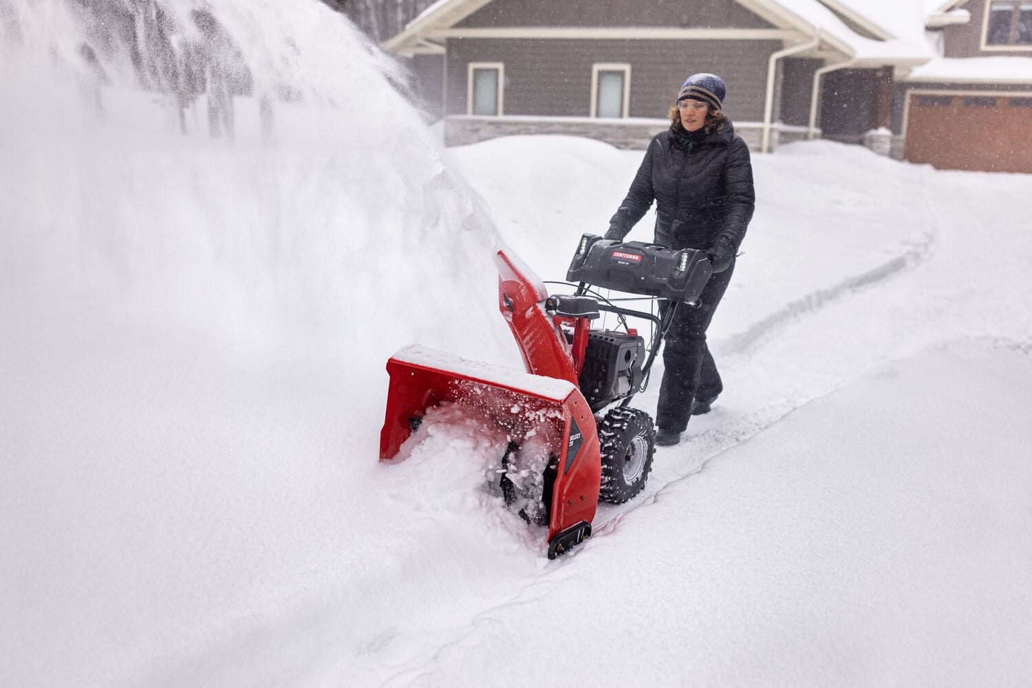 Photo d'une personne utilisant une souffleuse à neige Craftsman à l'extérieur par forte neige, SKU CMGB223101, dégageant une allée.