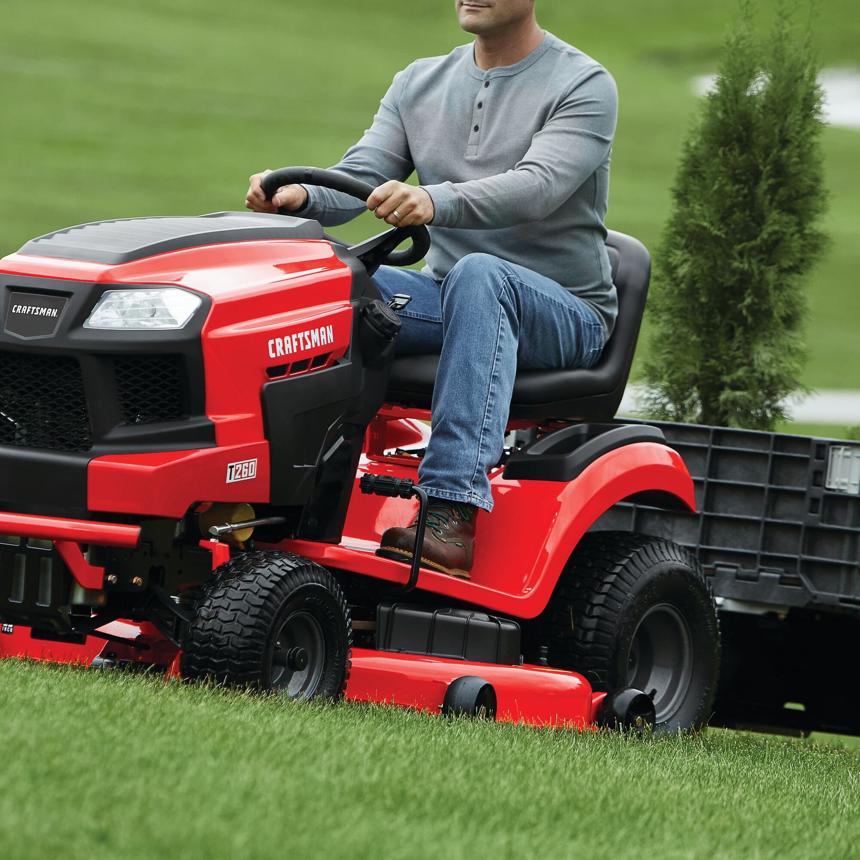 Photo du tracteur de pelouse Craftsman CMXGRAM1130045 rouge, vue de côté, tirant une remorque sur l’herbe.
