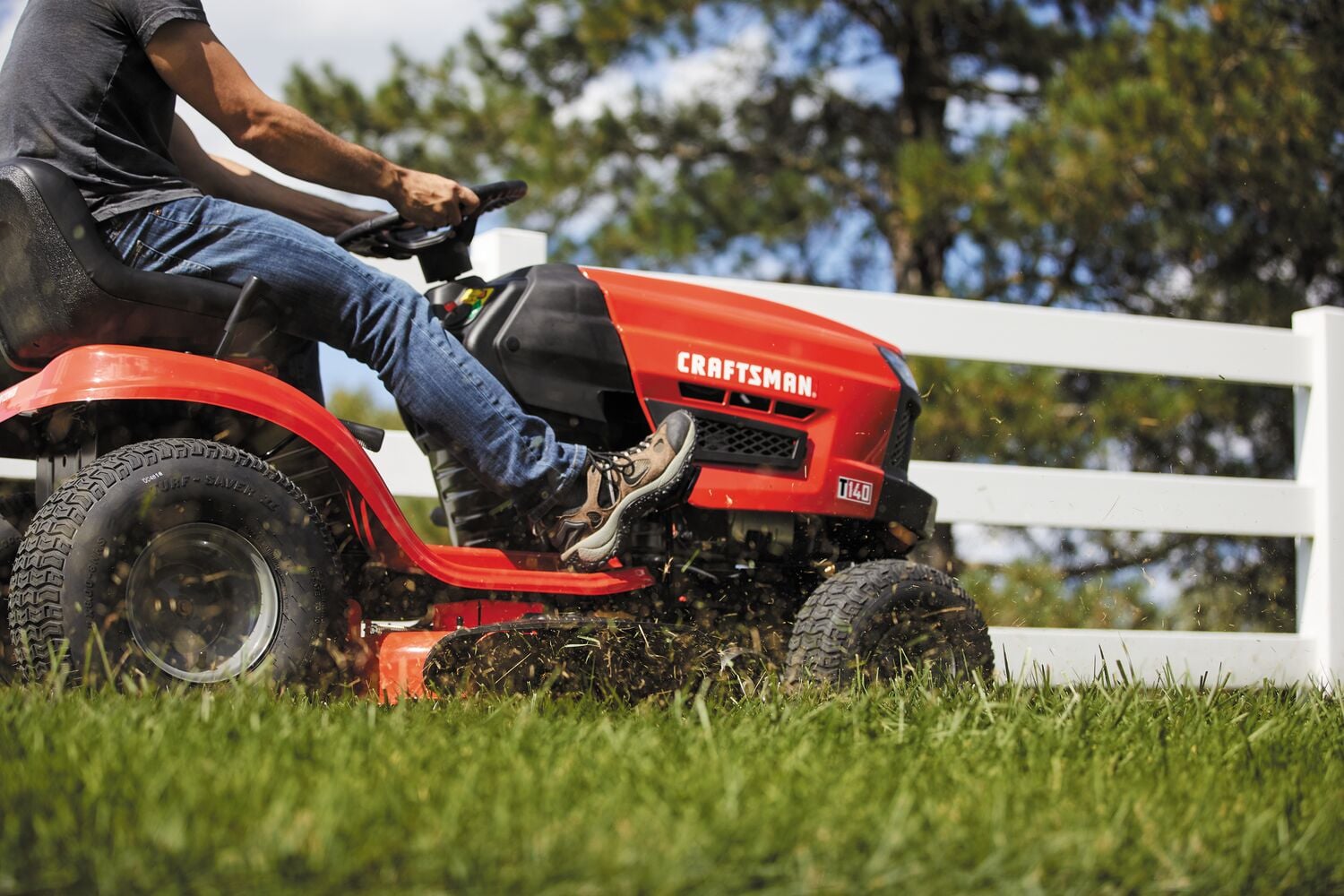 Photo of a Craftsman riding lawn mower, SKU CMXGRAM201305, side view in use on grass near a white fence outdoors.