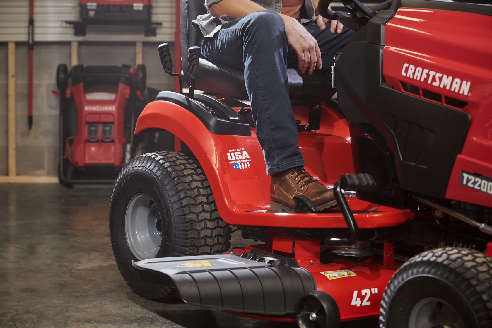 Photo of Craftsman riding lawn mower CM13APA9ZSA93, side angle, showing wheels and footrest in a garage.
