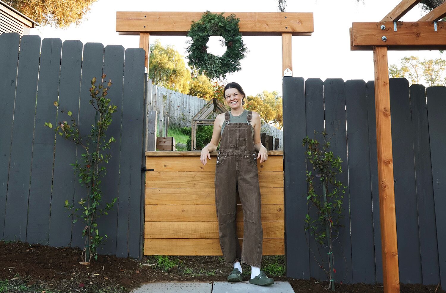 Woman wearing an overall leaning on a wooden fence creating a Trellis