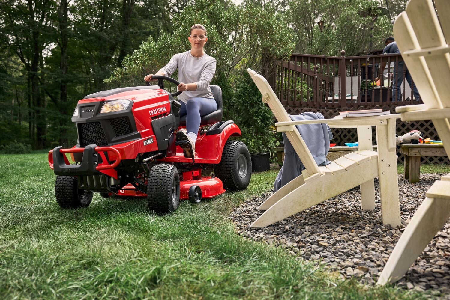 Photo of Craftsman riding lawn mower CM13APA9ZSA93 in use on green grass near outdoor chairs.