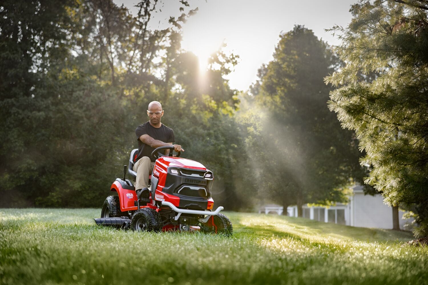 Photo of a person driving a red Craftsman riding lawn mower, SKU CMCRM233303, on grass with trees in the background.