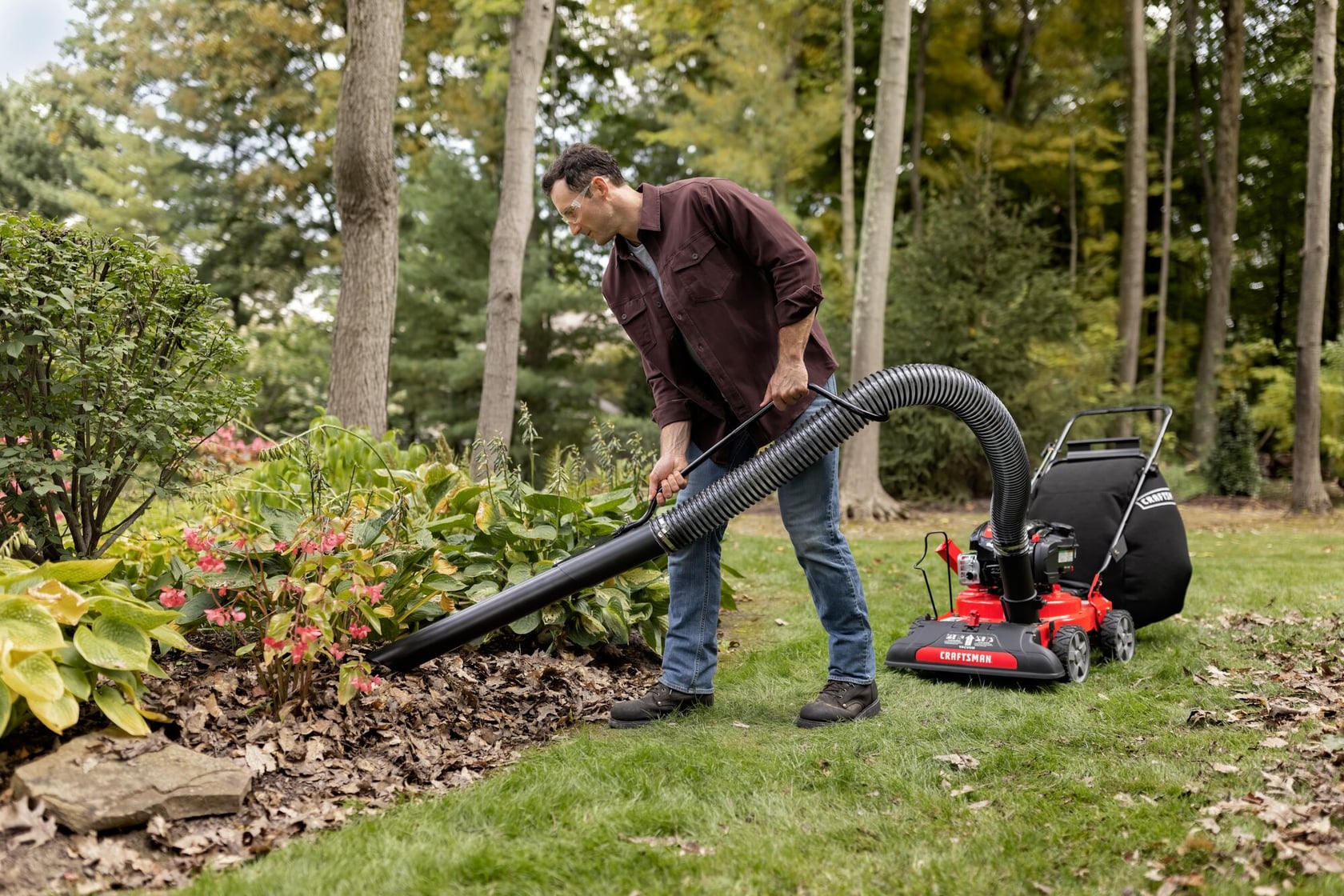 Photo d'une personne utilisant un aspirateur de pelouse Craftsman modèle CMXGPAM1080054 à l'extérieur pour ramasser des feuilles dans un parterre de fleurs.