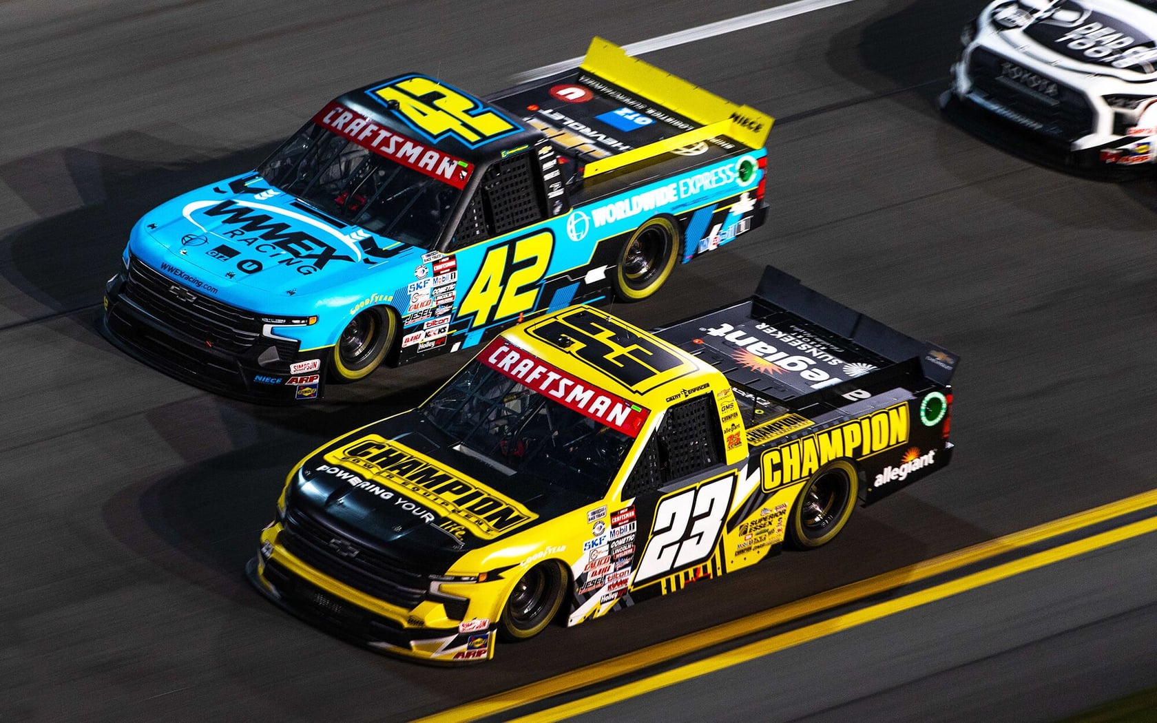 Photo de camions de course Craftsman, numéro 42 en bleu et numéro 23 en jaune, vue latérale sur piste.
