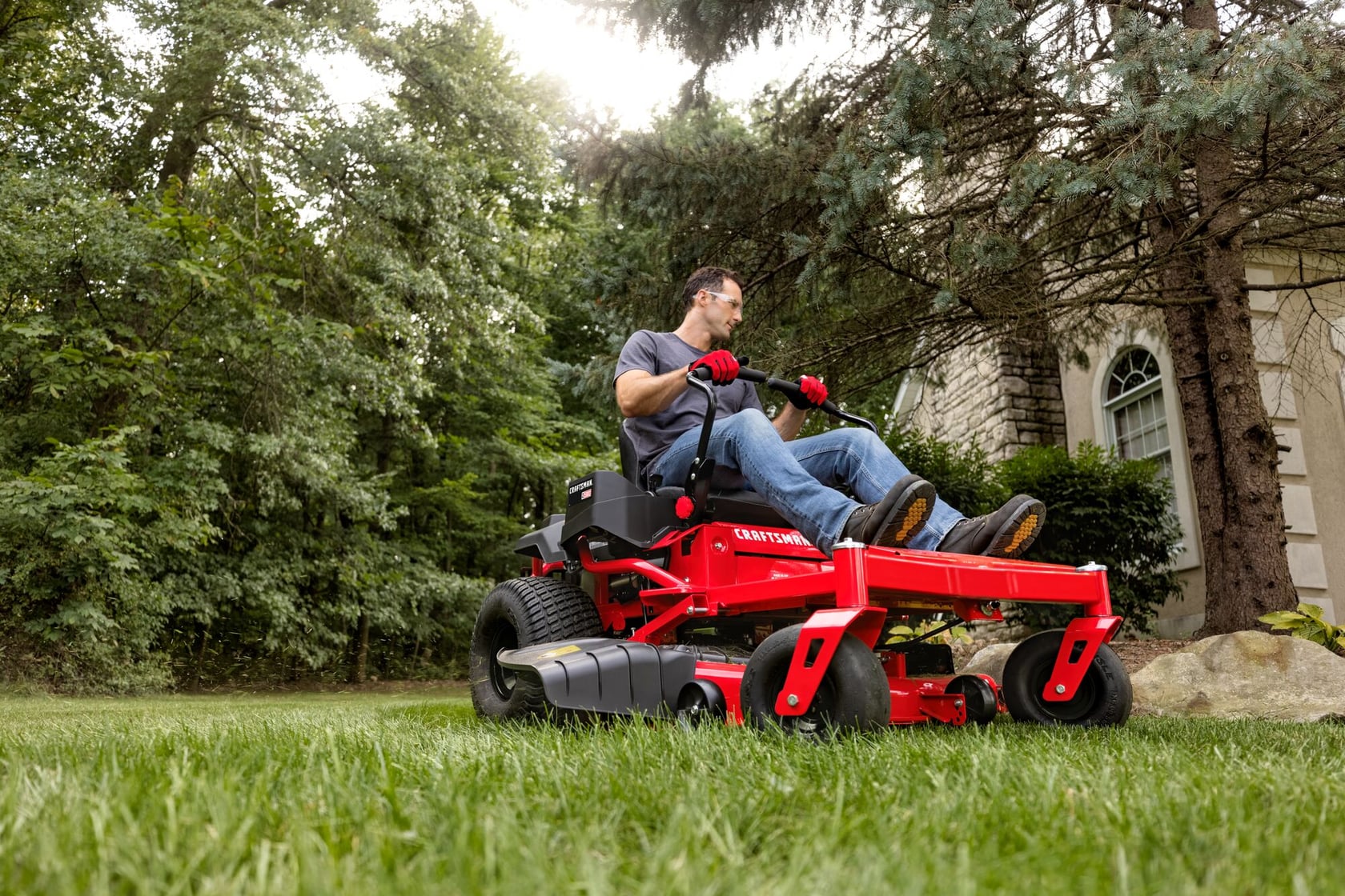 Tondeuse autoportée à rayon de braquage zéro Craftsman CMXGNAM211704 en utilisation à l'extérieur, vue latérale sur l'herbe près des arbres.