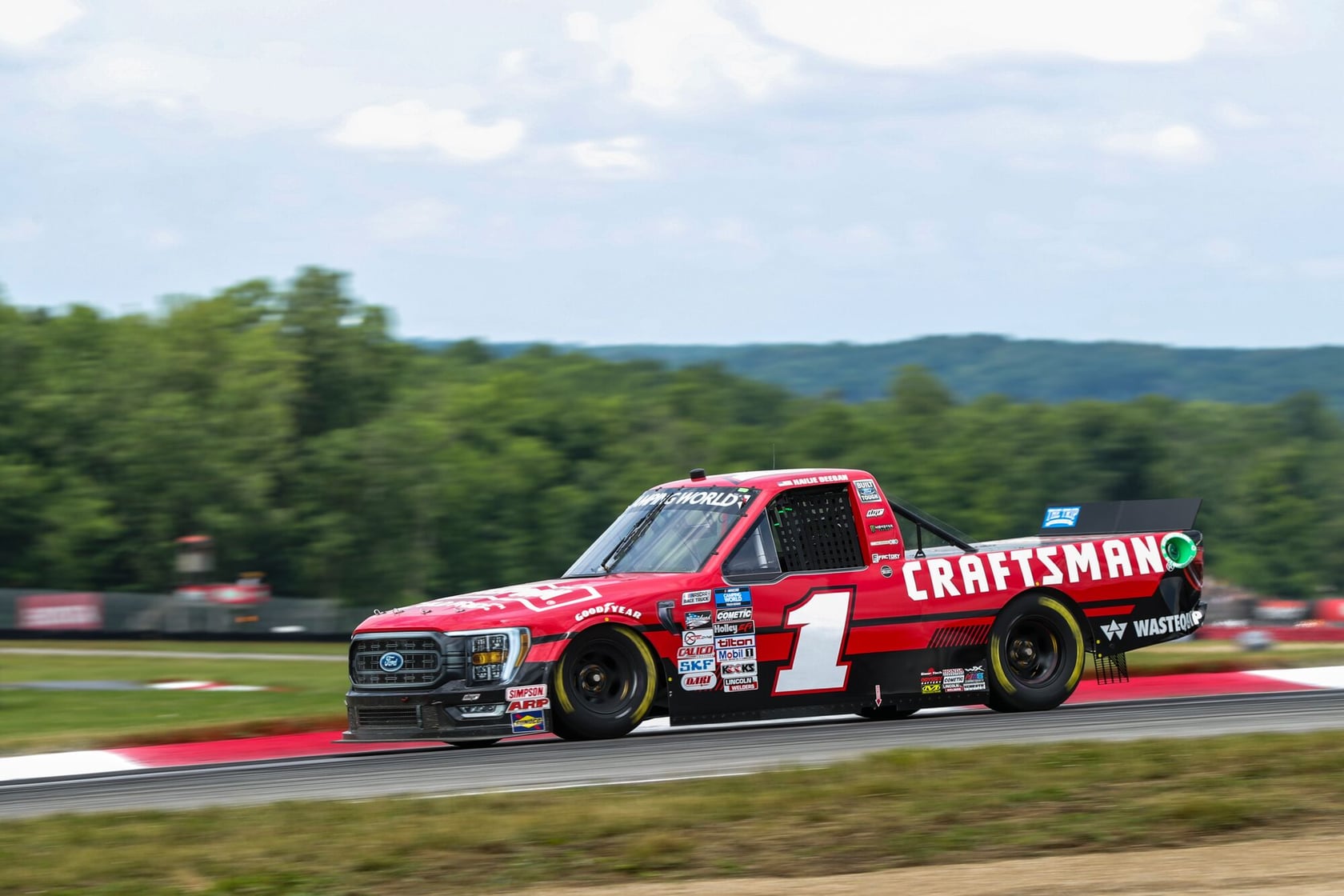 Photo d'un camion de course rouge marqué CRAFTSMAN, numéro 1, roulant sur une piste avec de la verdure en arrière-plan.