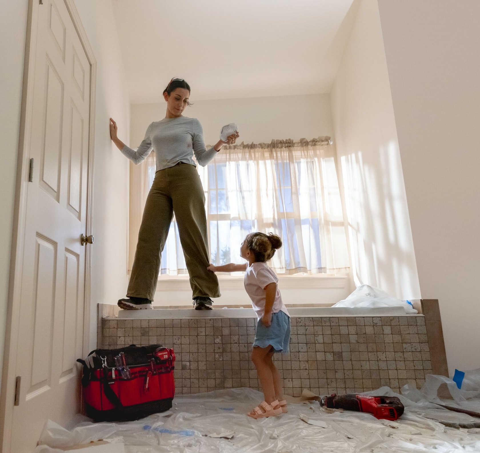 Daughter interrupting mother working on bathroom renovation with CRAFTSMAN tools in foreground.