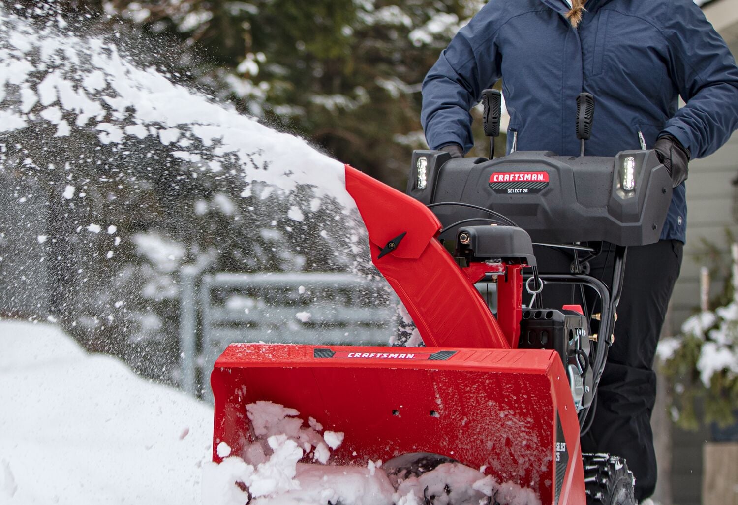 Photo de la souffleuse à neige rouge Craftsman CMXGBAM213102 en fonctionnement, éjectant de la neige, opérateur en veste bleue visible.
