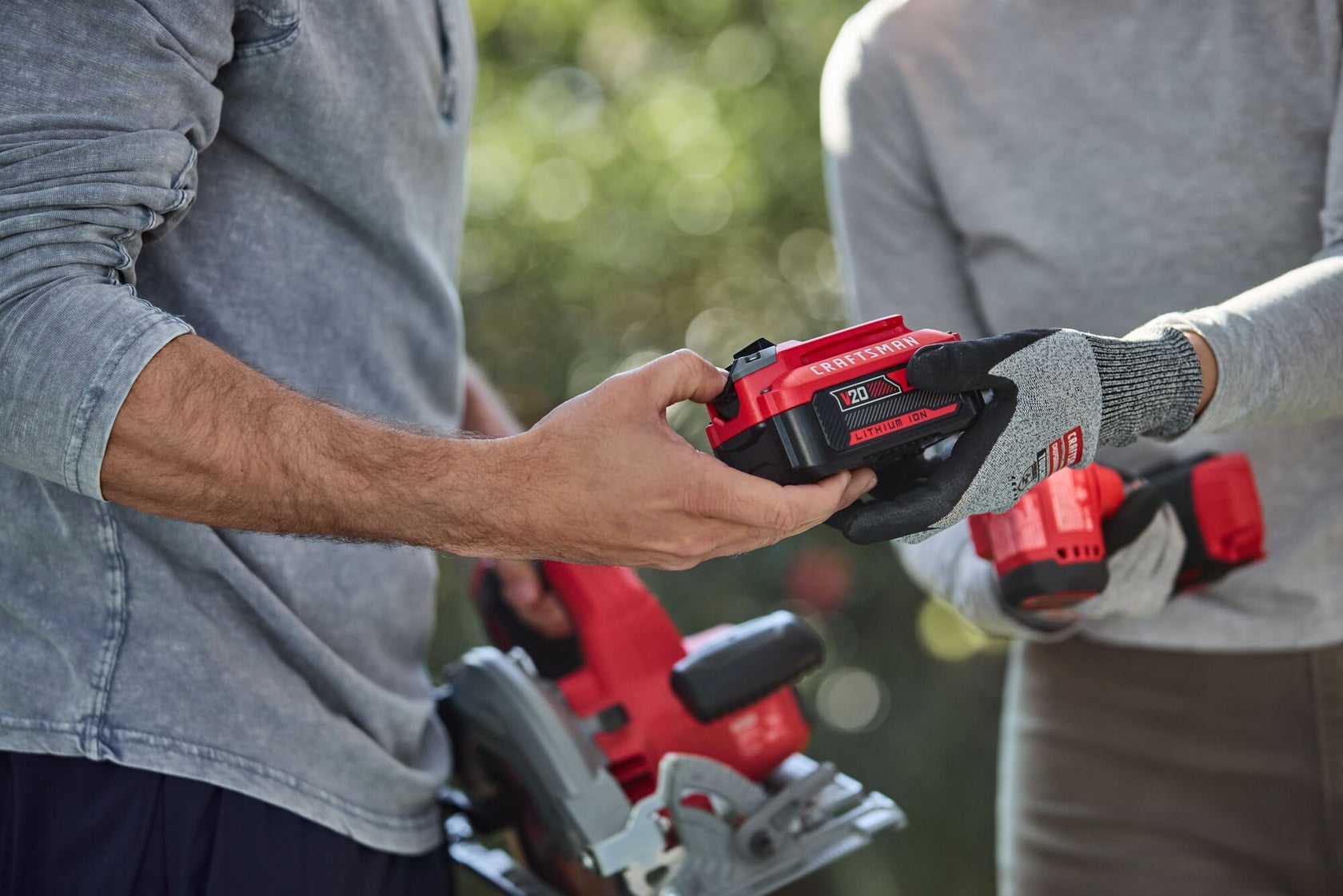Photo of Craftsman 20V battery CMCS551B being handed to person holding red power tool outdoors.