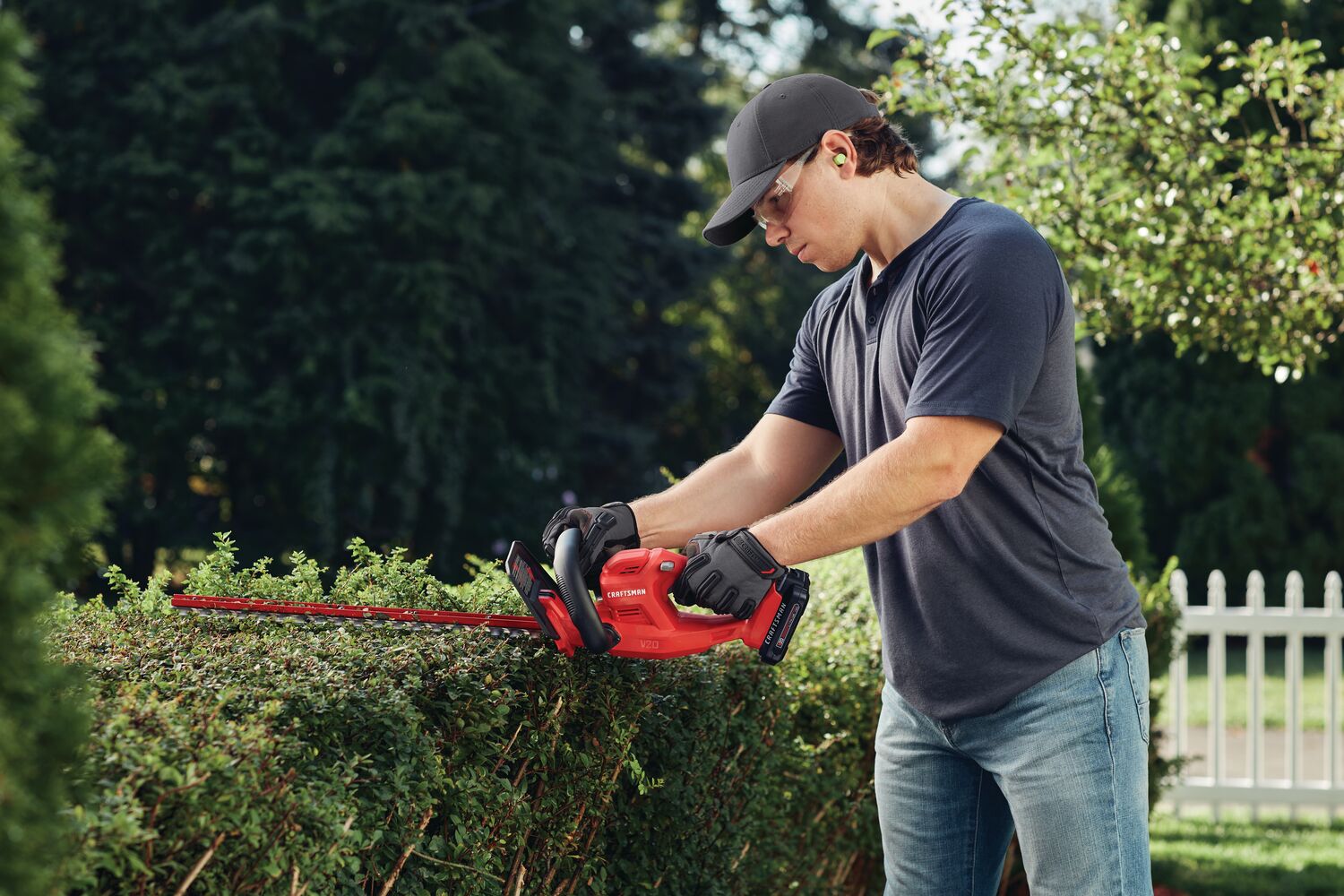 Cordless 20 inch hedge trimmer being used to level hedge by person.