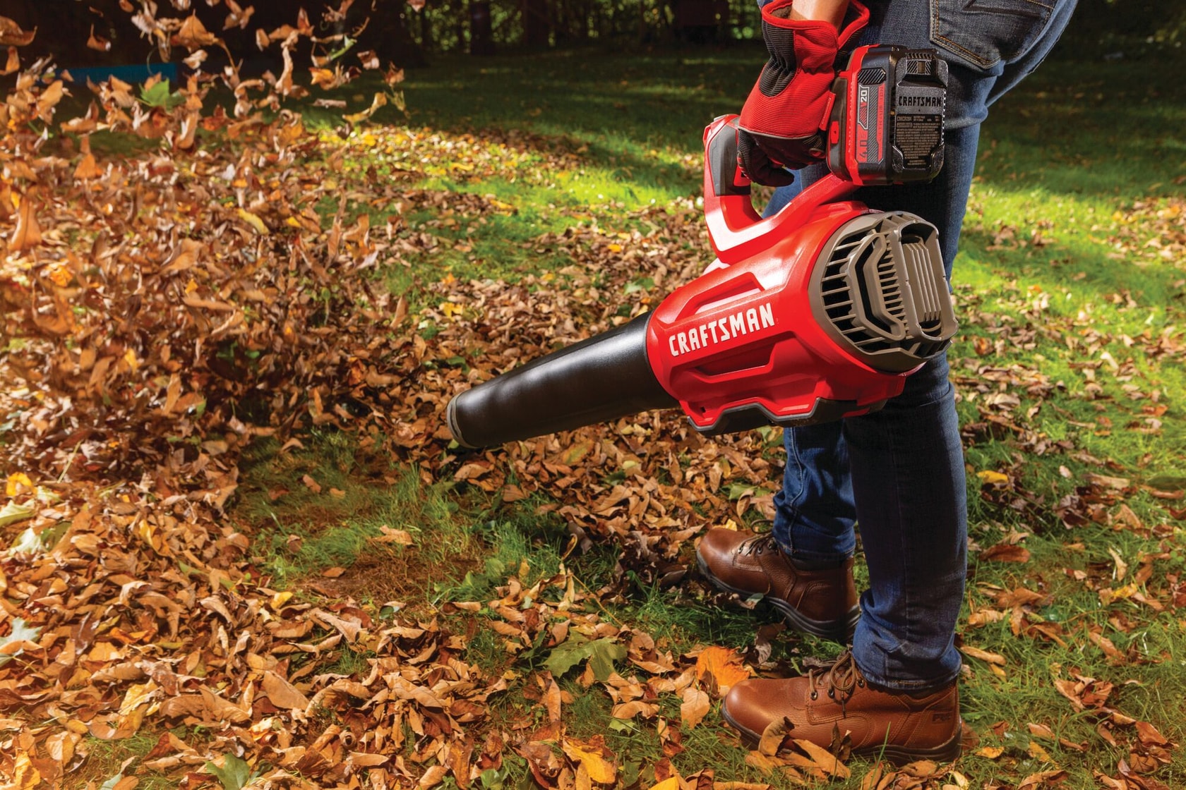 Brushless cordless axial blower being used for cleaning dead leaves from lawn.