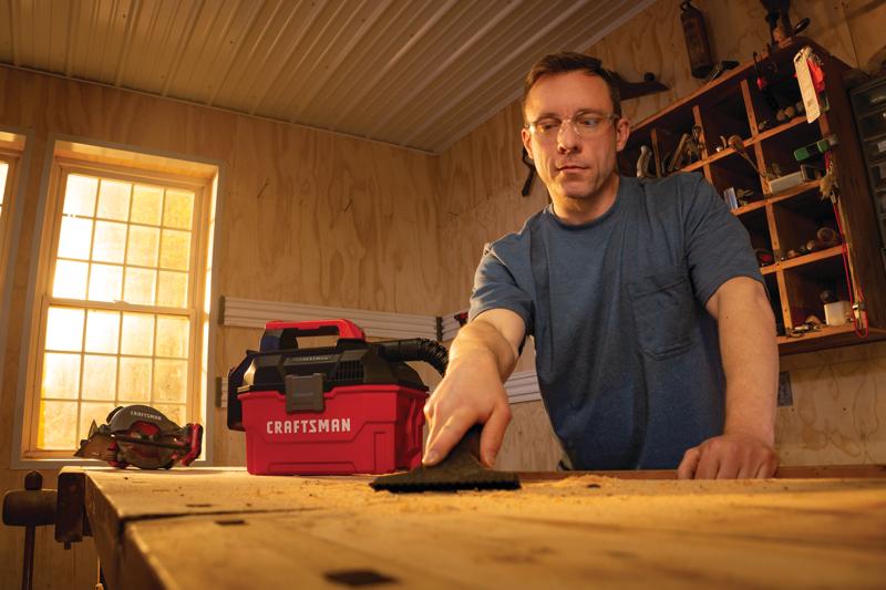 20 volt cordless 2 gallon wet dry vacuum being used by a person to clean wooden work station.