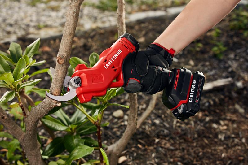 20 volt cordless pruner kit being used by a person to cut a branch outdoors.